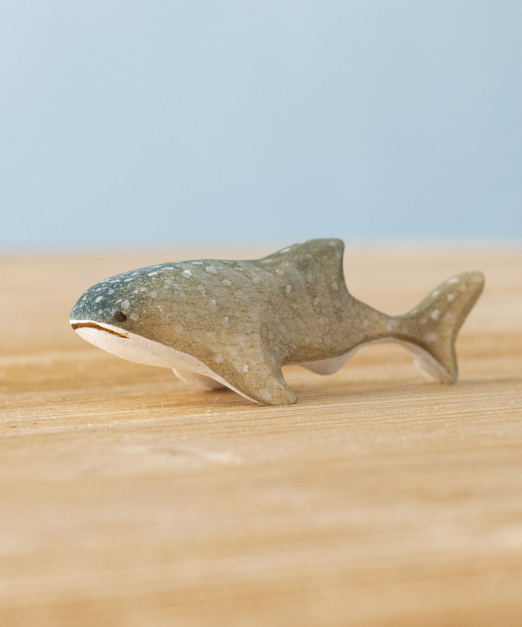 Bumbu handmade and hand painted wooden grey baby whale shark figure available at Babipur and resting on a wooden surface