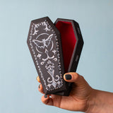 An adult hand holding the Bumbu handmade and hand painted wooden black coffin showing size