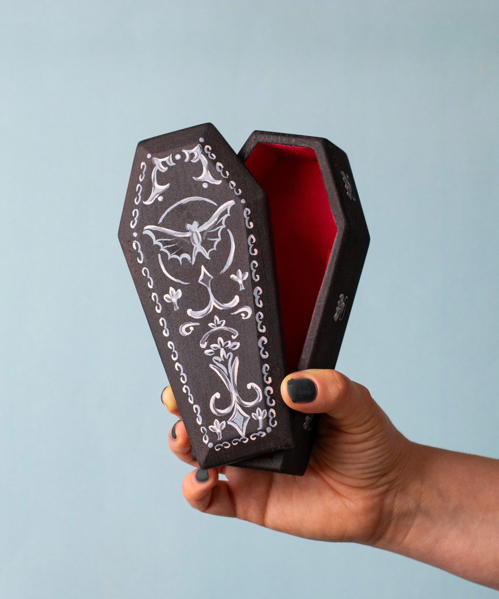 An adult hand holding the Bumbu handmade and hand painted wooden black coffin showing size