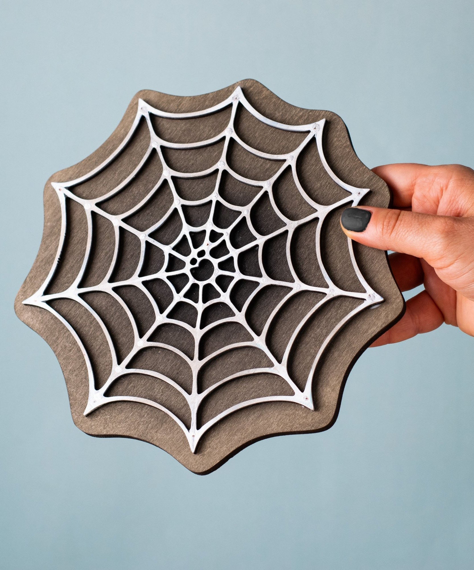 A hand holding the Bumbu handmade and hand painted white cobweb piece showing size