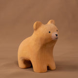 Bumbu handmade and hand painted wooden brown curious bear figure standing on a soft brown cloth