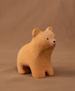 Bumbu handmade and hand painted wooden brown curious bear figure standing on a soft brown cloth