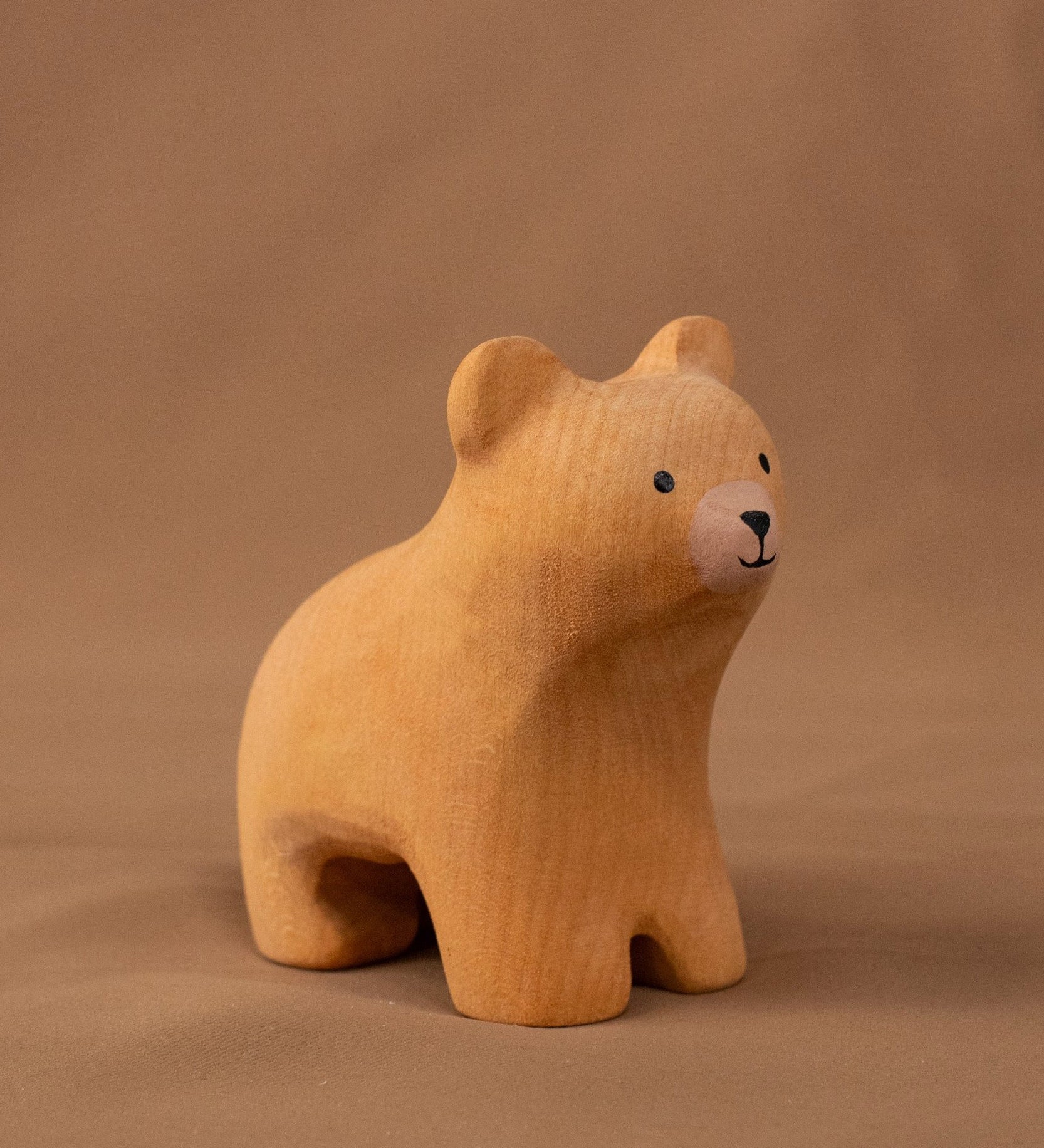 Bumbu handmade and hand painted wooden brown curious bear figure standing on a soft brown cloth