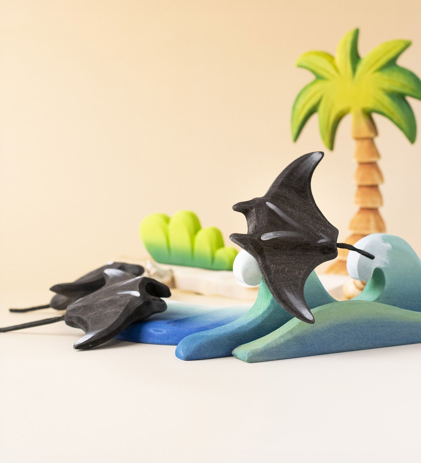 Bumbu handmade and hand painted wooden black manta ray figure available at Babipur and resting on a wooden wave piece with palm trees in the background.