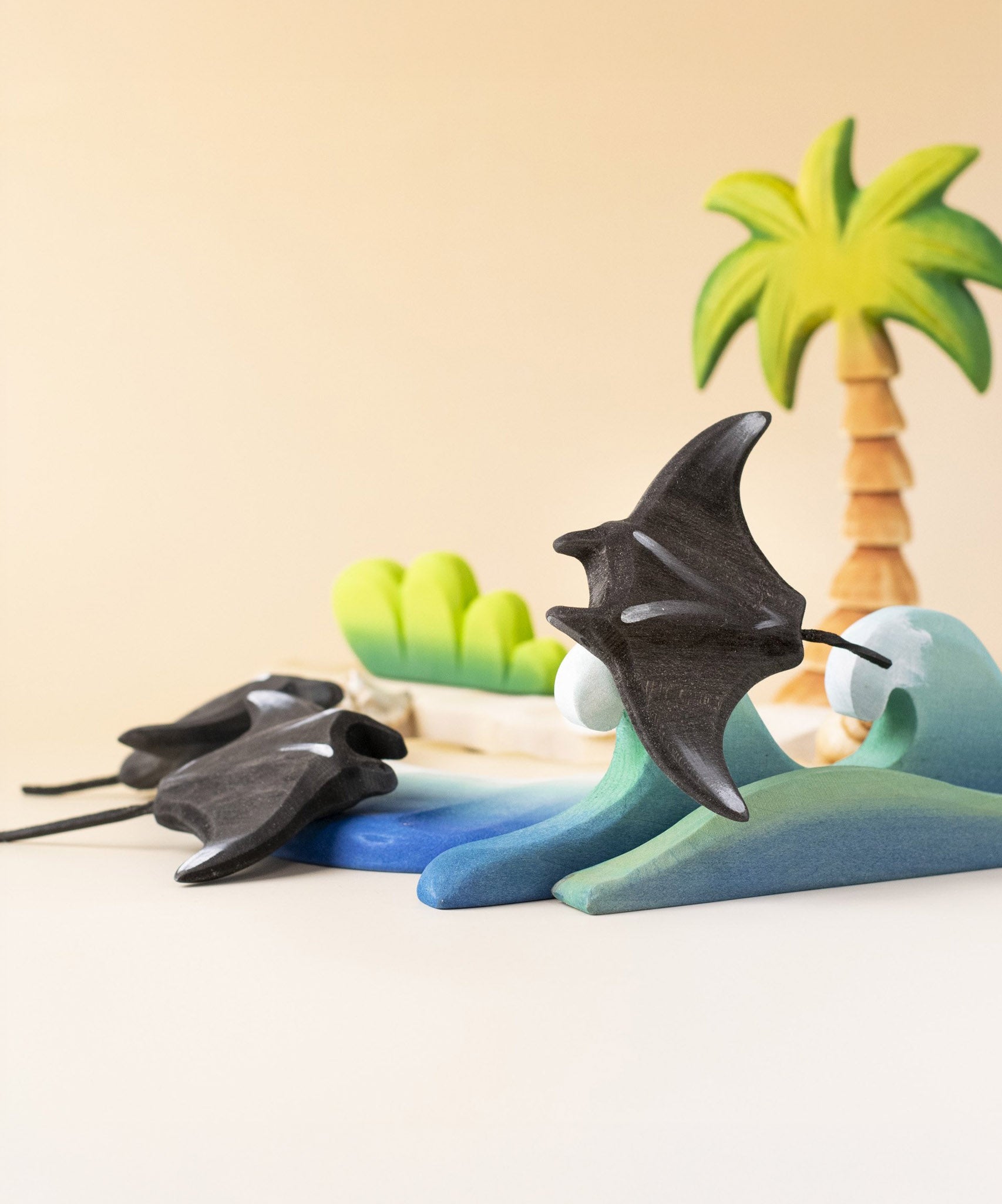 Bumbu handmade and hand painted wooden black manta ray figure available at Babipur and resting on a wooden wave piece with palm trees in the background.