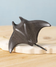 Bumbu handmade and hand painted wooden black manta ray figure available at Babipur and resting on a sandy island