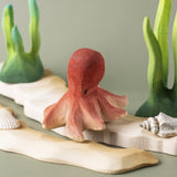 Bumbu handmade and hand painted wooden octopus figure resting on a wooden sandy piece and green coral figures