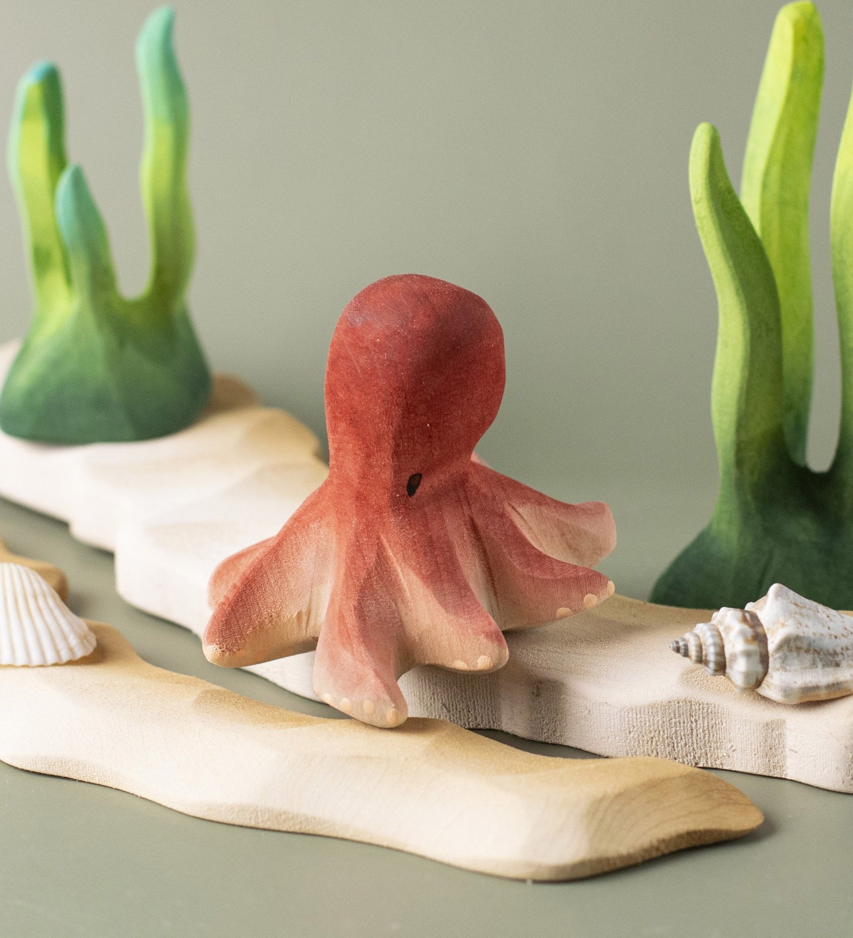 Bumbu handmade and hand painted wooden octopus figure resting on a wooden sandy piece and green coral figures