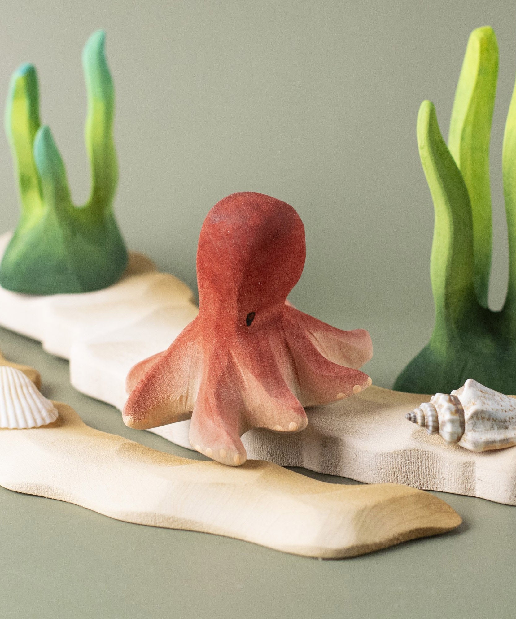 Bumbu handmade and hand painted wooden octopus figure resting on a wooden sandy piece and green coral figures