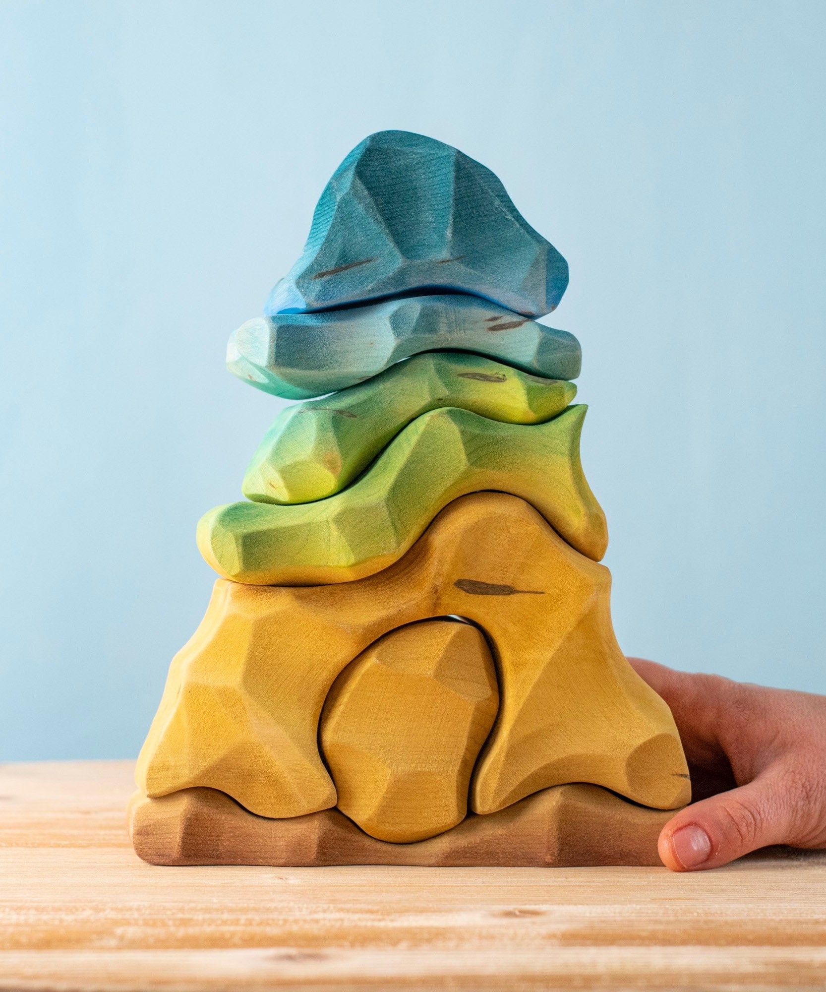 An adult hand holding the bottom of the Bumbu handmade and hand painted wooden reef set showing size