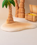 Bumbu handmade and hand painted wooden sandy island piece with a palm tree and treasure chest on top making a beach playscene