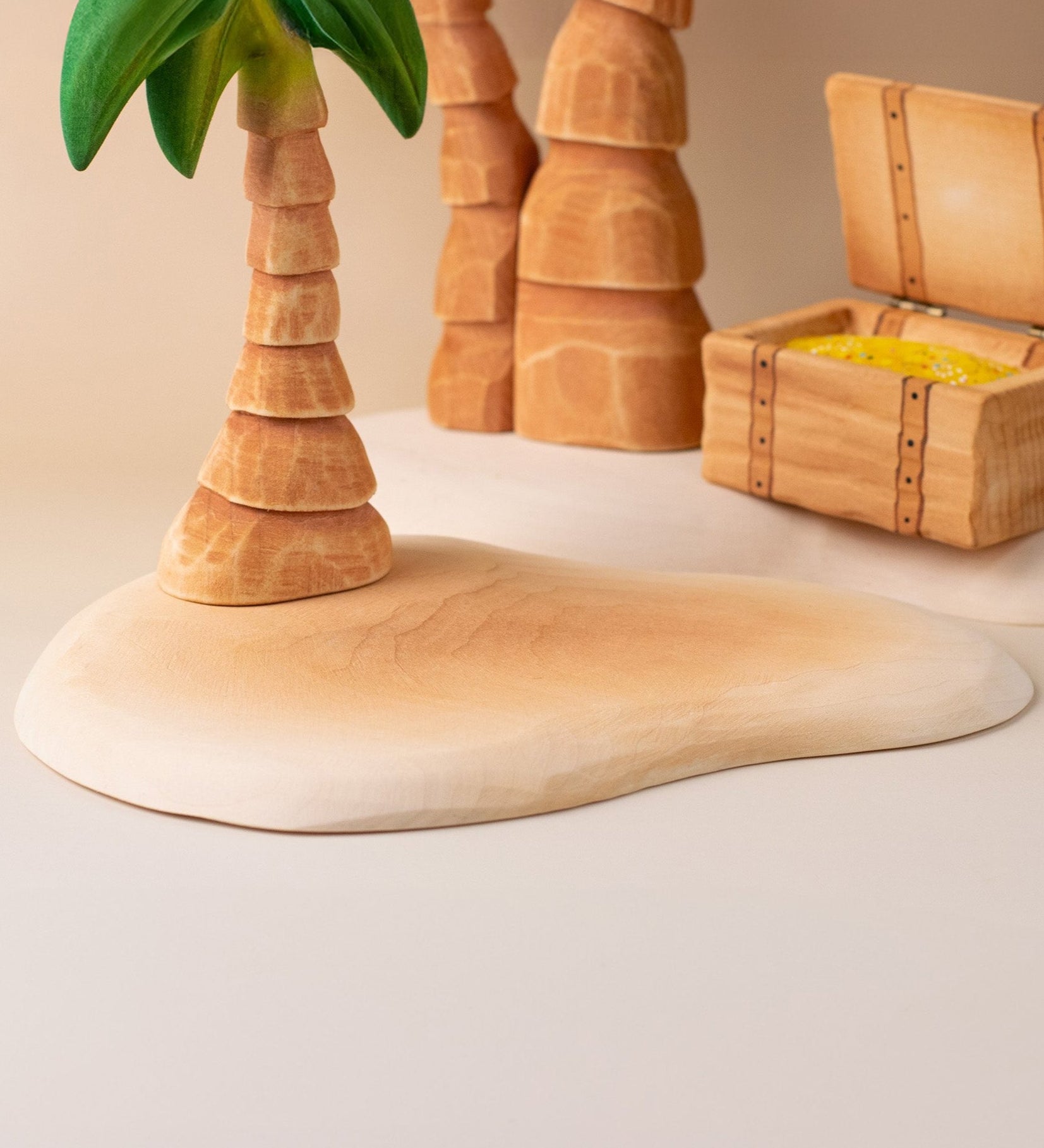 Bumbu handmade and hand painted wooden sandy island piece with a palm tree and treasure chest on top making a beach playscene