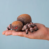 An adult hand holding the Bumbu handmade and hand painted wooden spider figure showing size