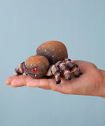 An adult hand holding the Bumbu handmade and hand painted wooden spider figure showing size