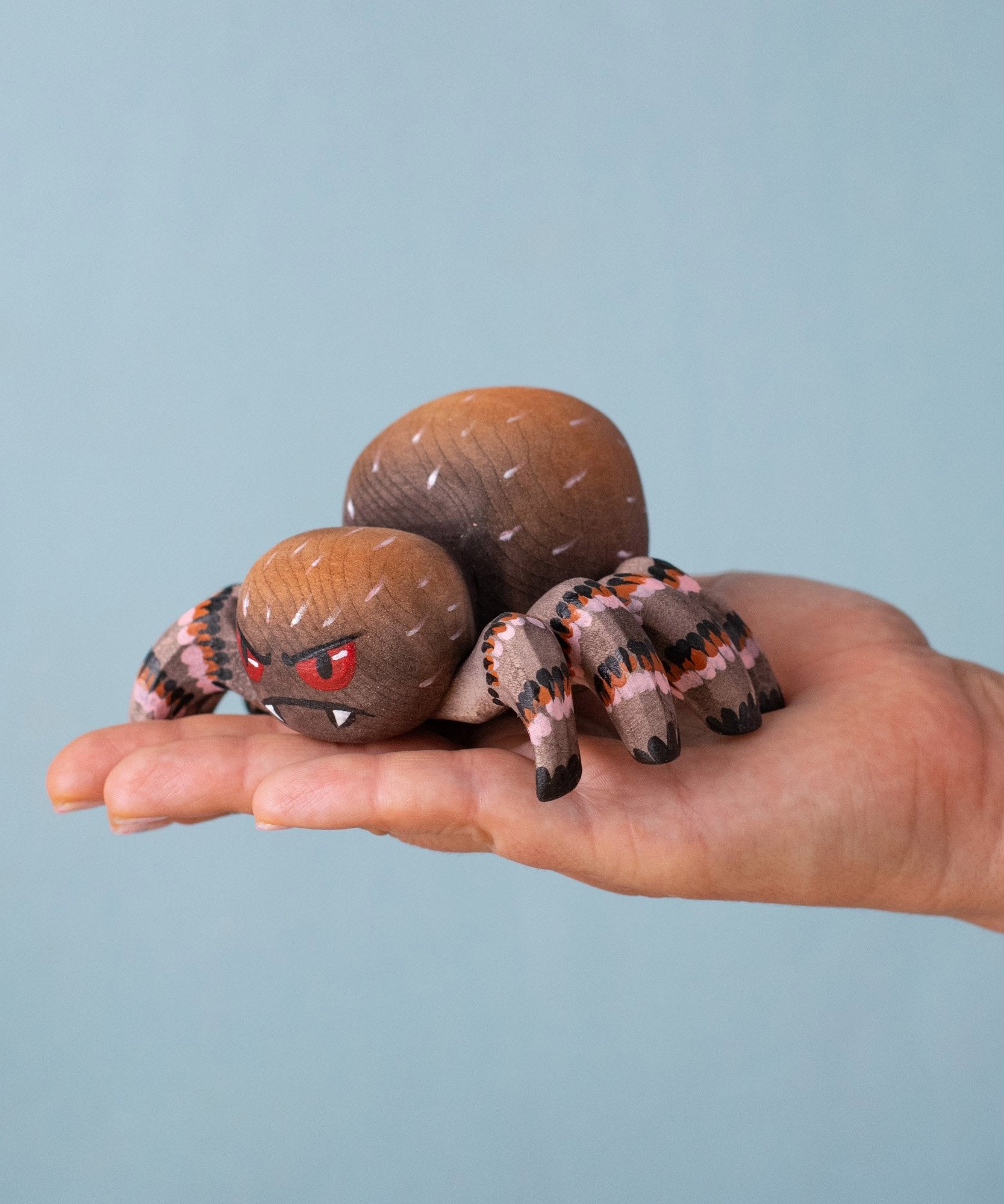 An adult hand holding the Bumbu handmade and hand painted wooden spider figure showing size