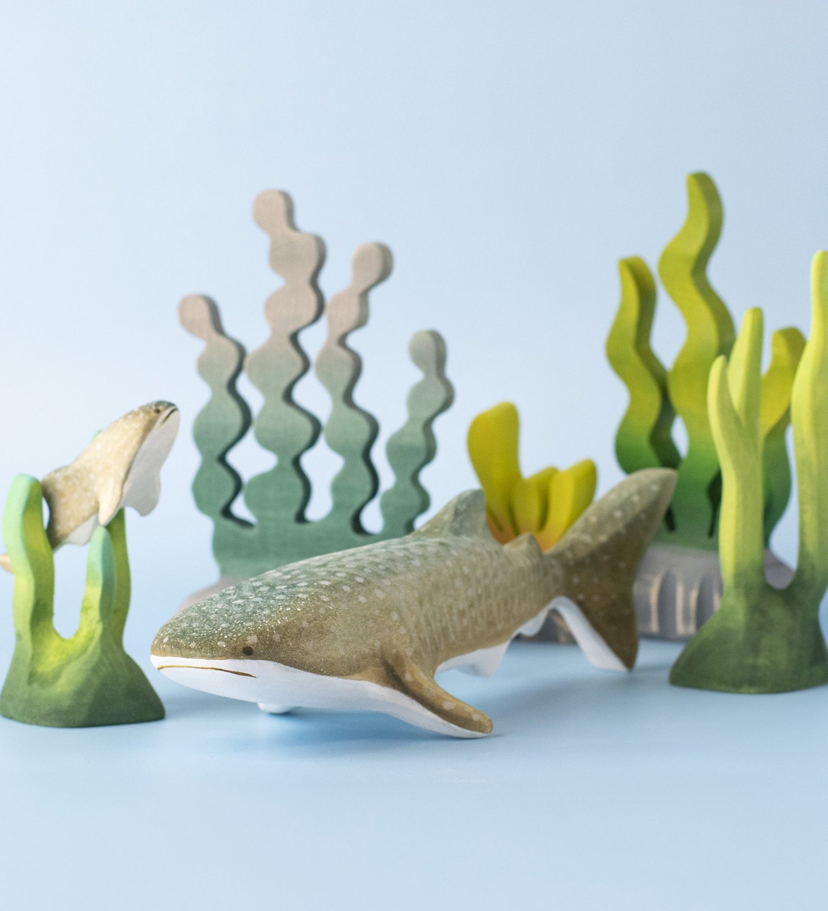 Bumbu handmade and hand painted wooden grey whale shark figure next to a swimming baby whale sark surrounded by Bumbu coral reef pieces available at Babipur.