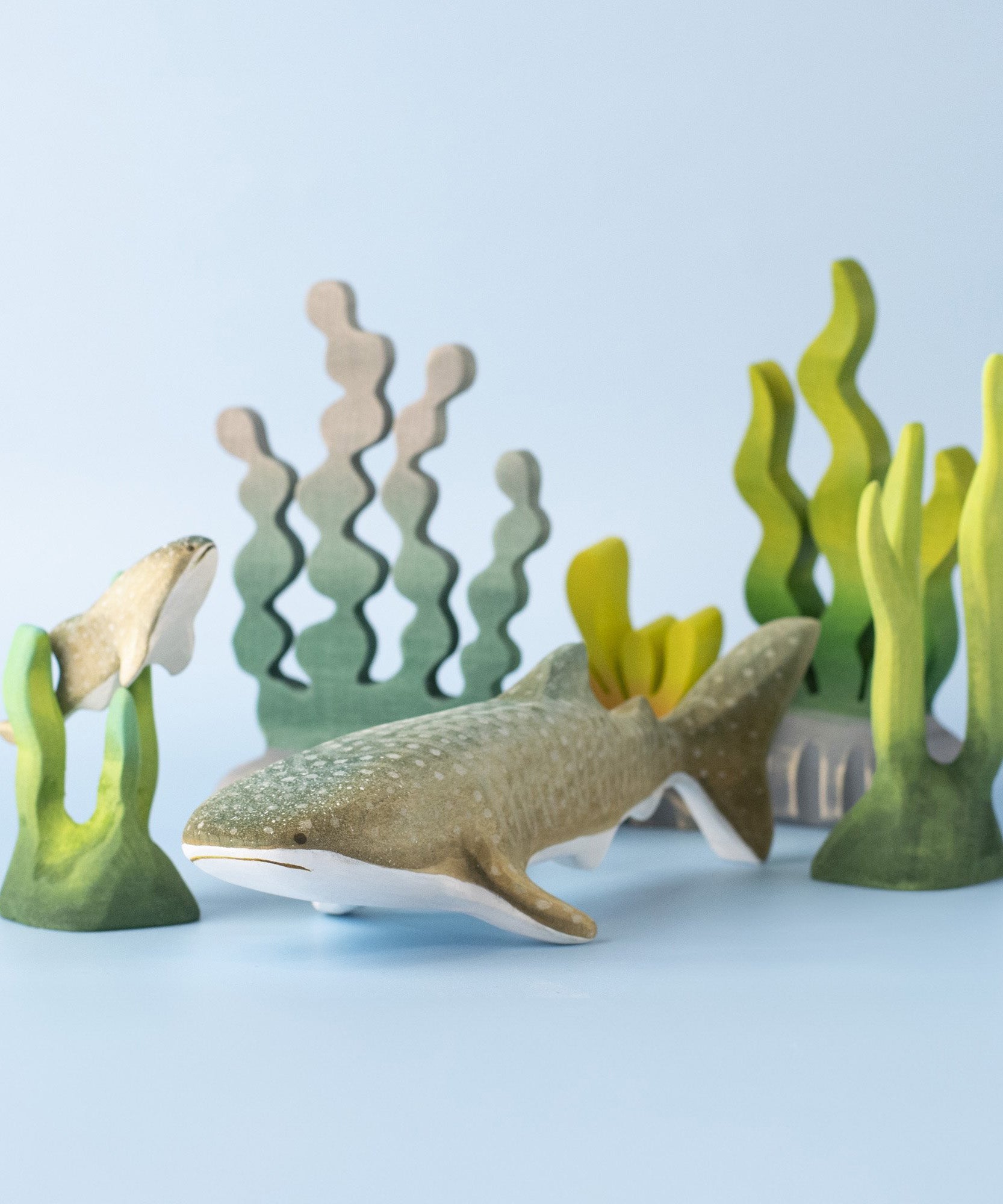 Bumbu handmade and hand painted wooden grey whale shark figure next to a swimming baby whale sark surrounded by Bumbu coral reef pieces available at Babipur.
