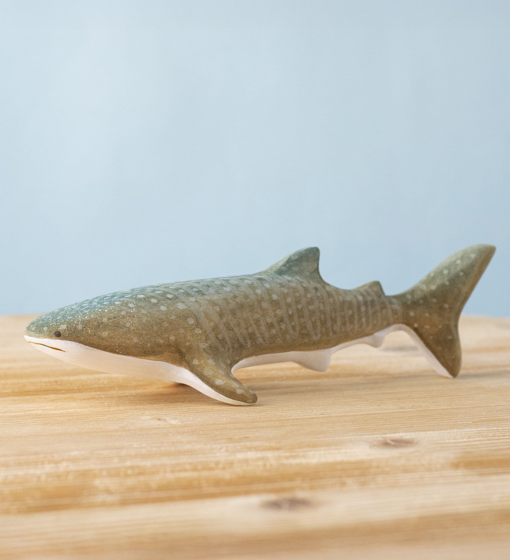 Bumbu handmade and hand painted wooden grey whale shark figure available at Babipur and resting on a wooden surface