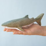 An adult hand holding the Bumbu handmade and hand painted wooden grey whale shark figure showing scale