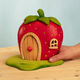 Adult hand holding Bumbu wooden strawberry house standing on a green base 