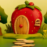 Bumbu wooden strawberry house standing on a green base and ladybird on top in a playscene with trees, grass and flowers