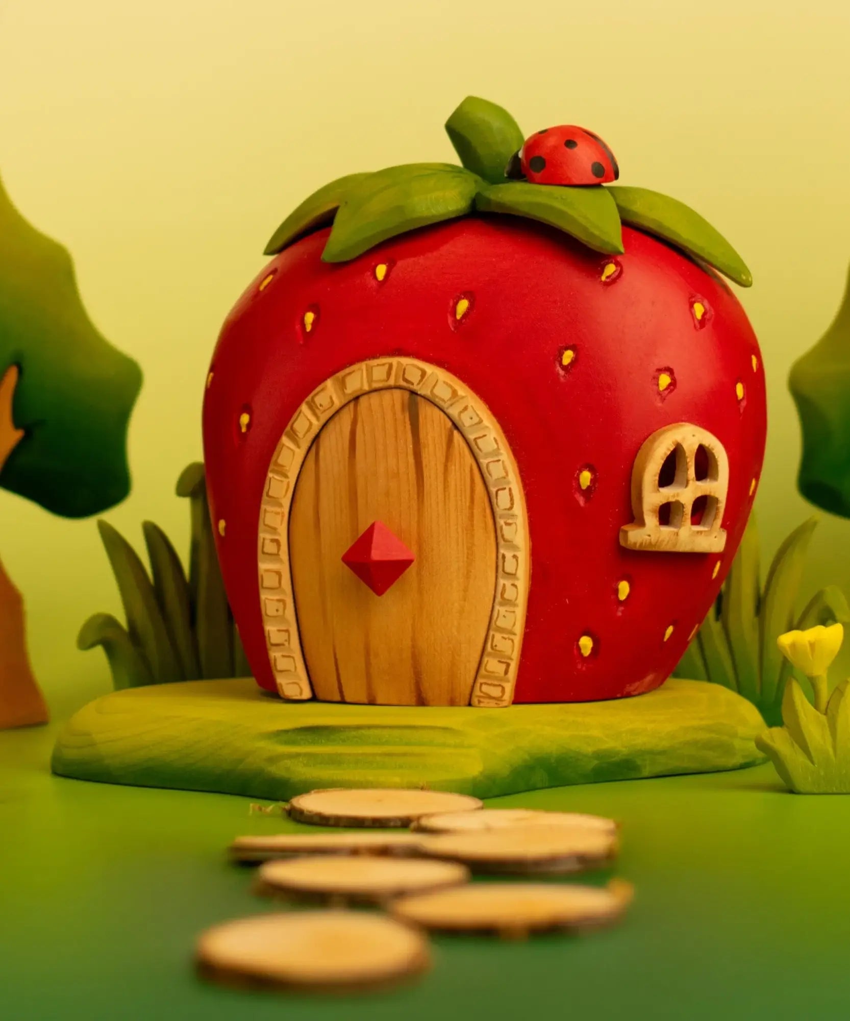 Bumbu wooden strawberry house standing on a green base and ladybird on top in a playscene with trees, grass and flowers
