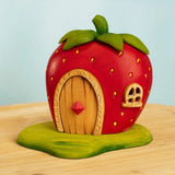 Strawberry-shaped toy house with wooden door on a light blue background