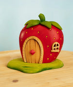 Strawberry-shaped toy house with wooden door on a light blue background