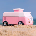 Candylab VW Beach bus in pink, stood on a sandy beach with a blue sky background