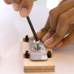 A person putting a screw and metal base into a Candycar wooden block, to make their own toy vehicle. The person is using a black alan key to turn the screw