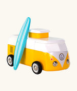 The Candylab VW Beach bus in yellow, with a wooden blue and white stripe surf board propped up next to the van, The image is on a cream background