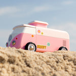 A side view of the Candylab VW Beach bus in pink with colourful stickers on the side of the van, stood on a sandy beach with a blue sky background