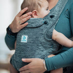 A child being carried in the Carifit+ Baby Carrier in Cool Grey. The child is facing inwards towards the adult