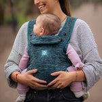 A person carrying a child in the Carifit+ Baby Carrier in Cool Green. The child is facing inwards towards the adult.