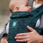 A child facing inwards whilst being carried in the Carifit+ Baby Carrier - Cool Green. The image offers a closer look at the material detailing and the removable head and neck support
