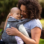 An adult carrying a child inside the Carifit+ Fabric Baby Carrier in Grey. The child is inwards facing towards the adult