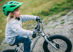 Child wearing a green helmet and gray jacket riding Early Rider's Belter 16 inch wheel children's bike on a gravel path.