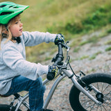 Child wearing a green helmet and gray jacket riding Early Rider's Belter 16 inch wheel children's bike on a gravel path.