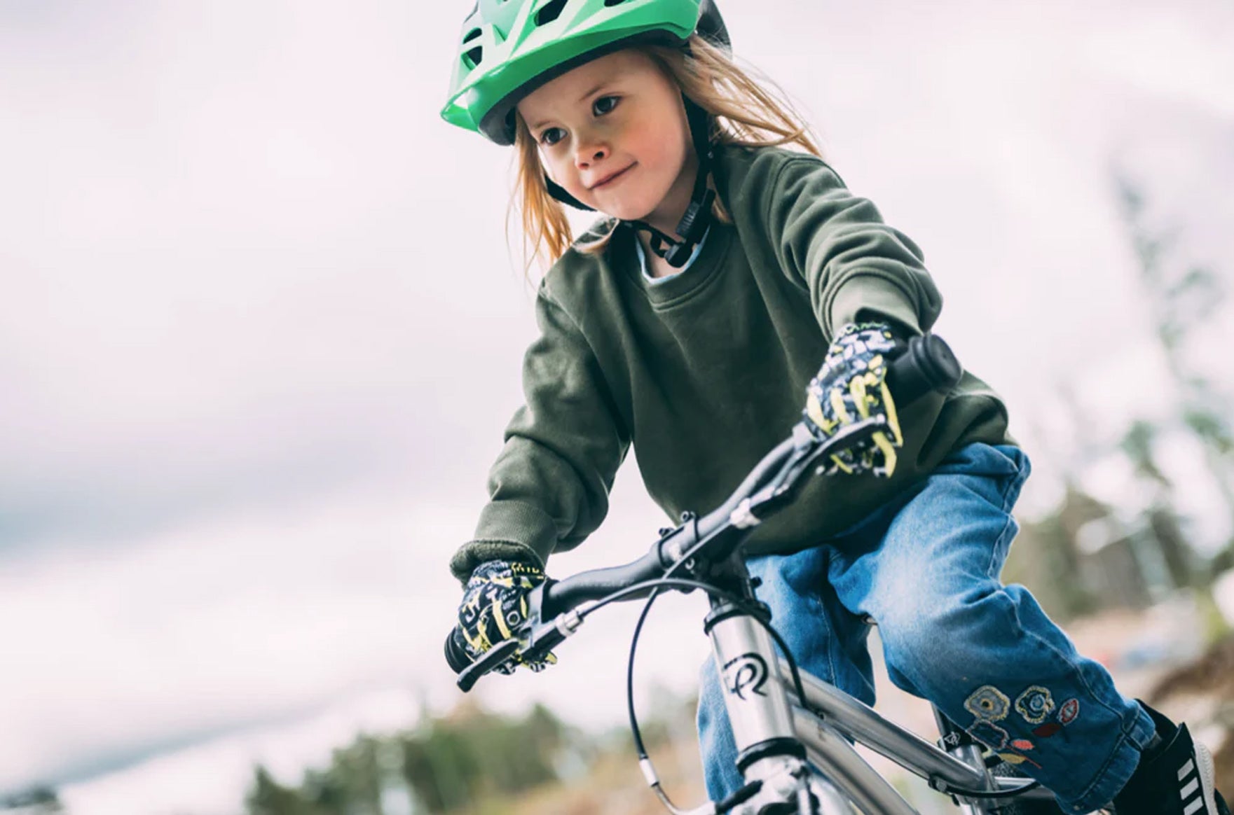 Child smiling while riding a bicycle outdoors and wearing a green helmet