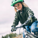 Child smiling while riding a bicycle outdoors and wearing a green helmet
