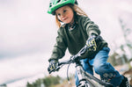 Child smiling while riding a bicycle outdoors and wearing a green helmet