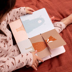 Child sat on a red blanket looking at the Trixie Flip-Flap Animals Book