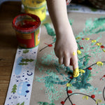 Child creating art with Okonorm finger paints. The child is dotting yellow and red paint to create Christmas tree lights.