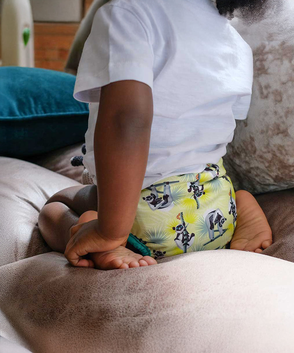 A little child wearing The Close Parent Pop-in reusable nappy wrap cover with velcro closures, in a lemur print