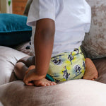 A little child wearing The Close Parent Pop-in reusable nappy wrap cover with velcro closures, in a lemur print