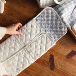Avery Row Travel Changing Mat - Coastline in adults hands, unfolded on a wooden table.