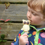 Cocoa Loco Fairtrade white chocolate owl lolly in hand of young boy outside. He's in a garden and is wearing a dark blue, vegetable patterned fleece.