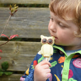 Cocoa Loco Fairtrade white chocolate owl lolly in hand of young boy outside. He's in a garden and is wearing a dark blue, vegetable patterned fleece.