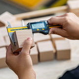 A person measuring a wooden block for a Cuboro block piece, using a handheld electronic measuring tool