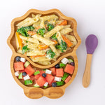 Eco Rascals Dinosaur Bamboo Suction Plate with pasta, carrots and broccoli and a watermellon side salad, and purple silicone and bamboo baby spoon.